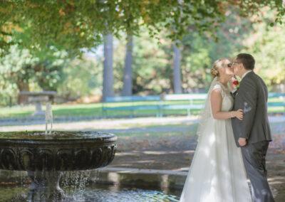 Kuessendes Brautpaar neben Brunnen im Schlosspark Weinberg
