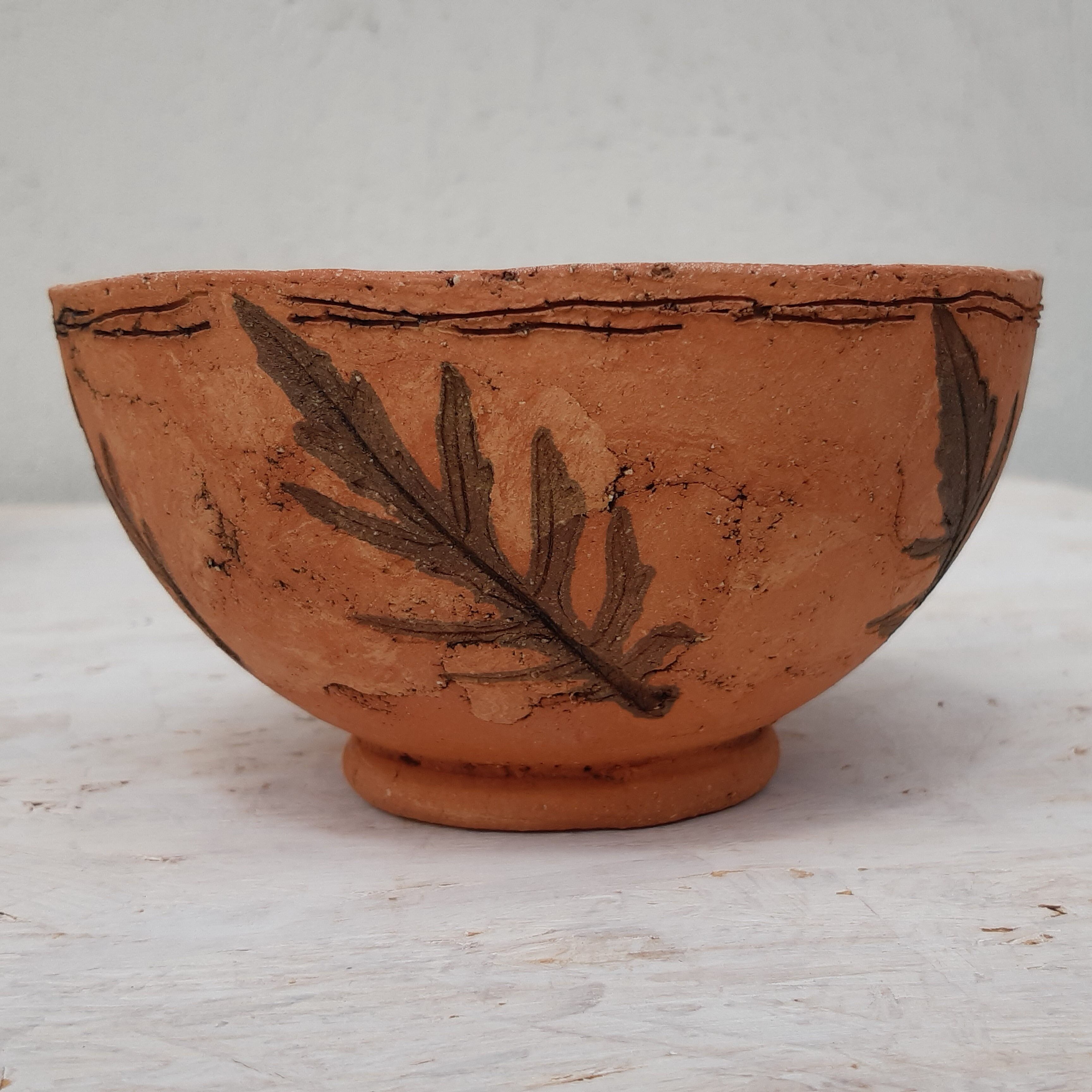 Terrakotta-Keramik mit eingefärbten Tonen, (c) Nikola Jakadofsky Braune Terrakotta-Keramikschale mit eingraviertem Blattmuster auf grauen Hintergrund.